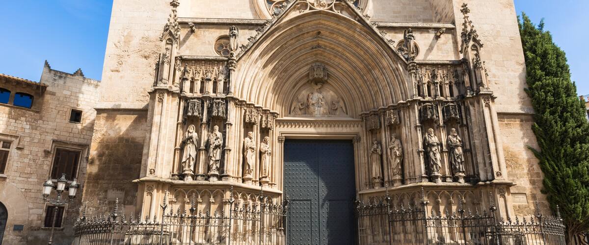 A historic cathedral with a large arched entrance, intricate stone carvings, and a prominent stained glass window.