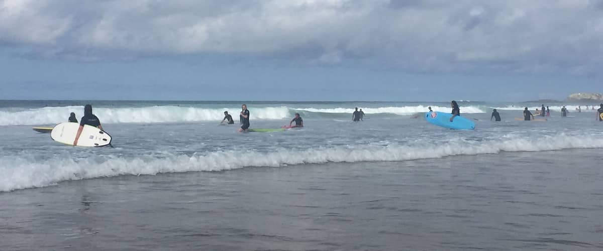 A beach with surfers and swimmers under a cloudy sky.