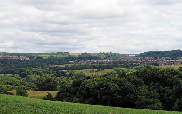 A rural landscape with rolling hills, a village in the distance, and a clear sky.