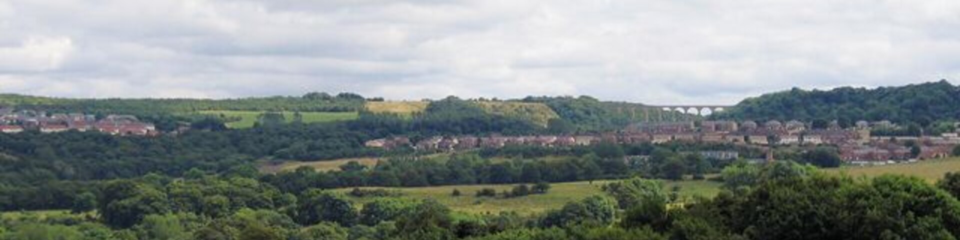 A rural landscape with rolling hills, a village in the distance, and a clear sky.