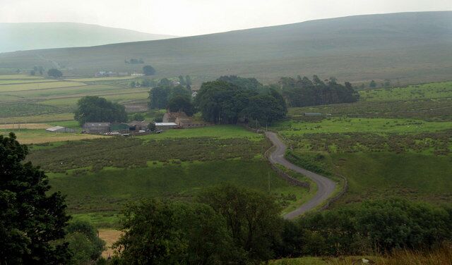 A winding country road through a rural landscape with fields, scattered trees, and a few buildings.