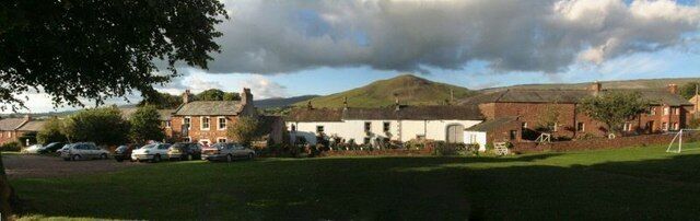 A rural village with houses, a grassy field, and a hill in the background.