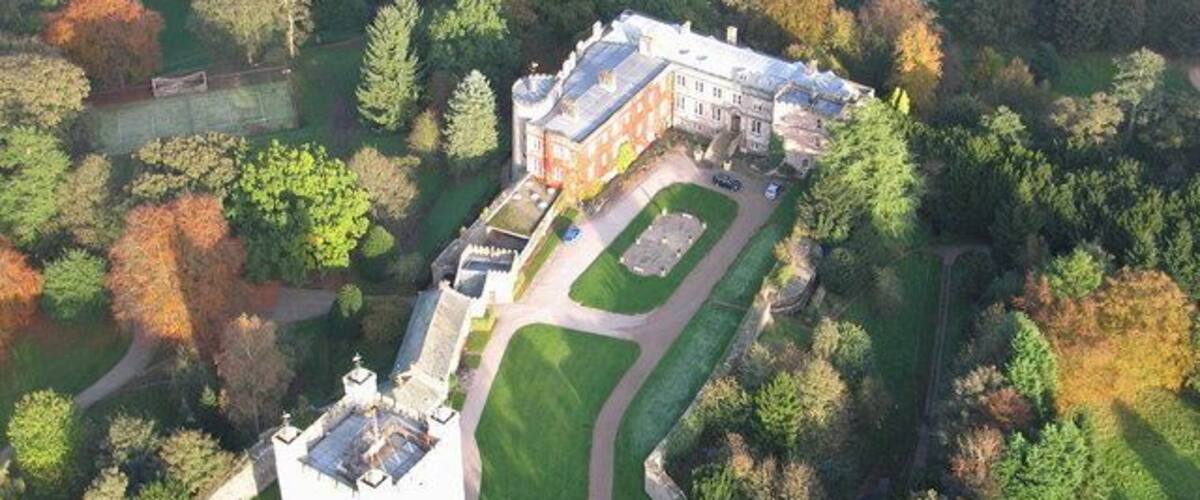 An aerial view of a castle surrounded by a park with a moat and a large lawn.