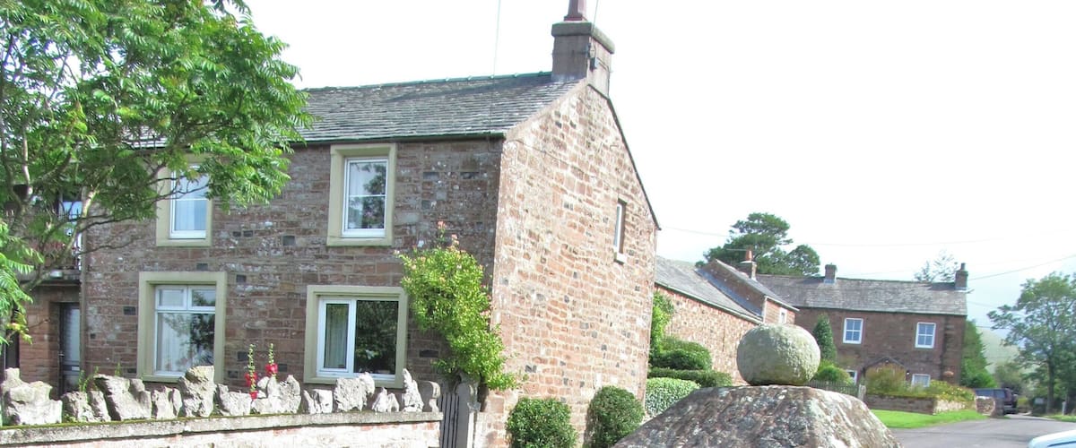 A stone monument in a grassy area with a brick house in the background.