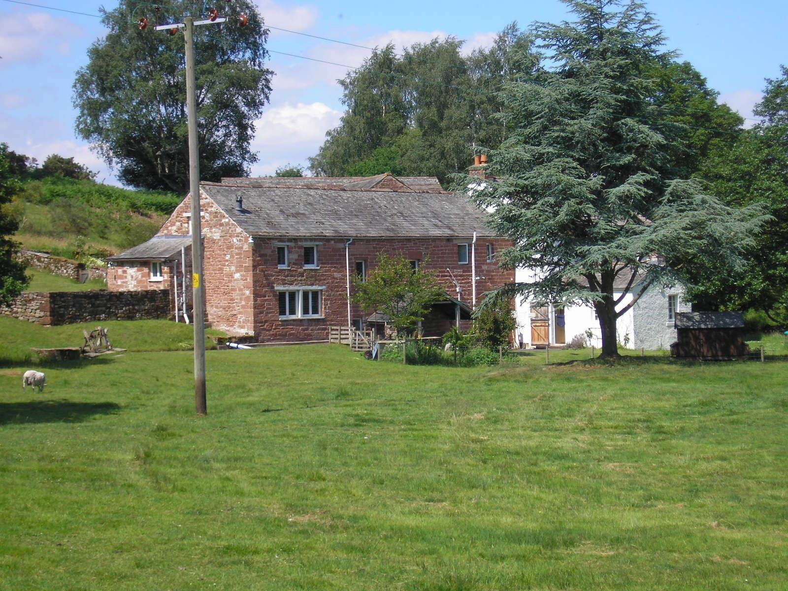 A stone house with a sloped roof, surrounded by a grassy field and trees.