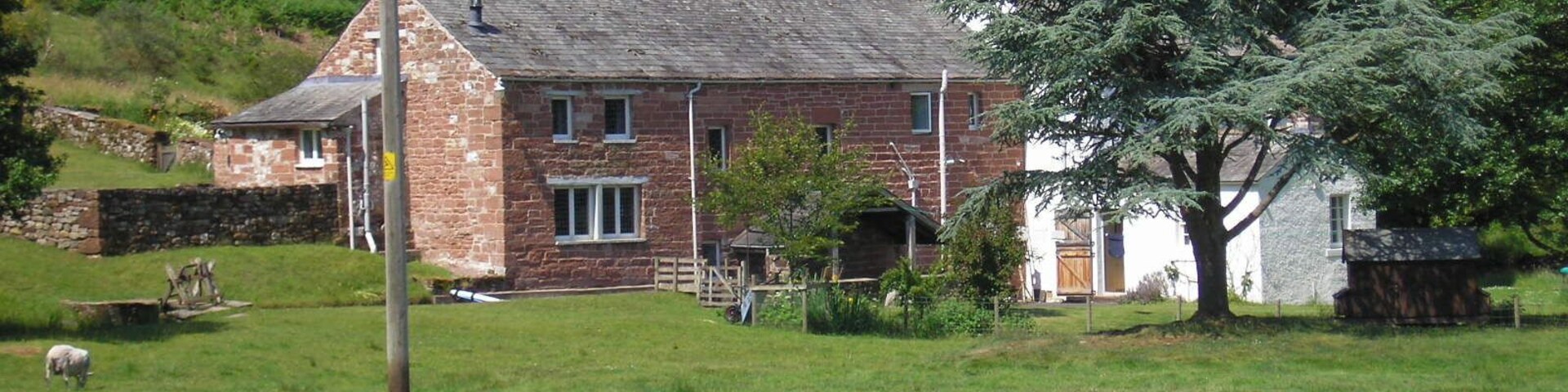 A stone house with a sloped roof, surrounded by a grassy field and trees.