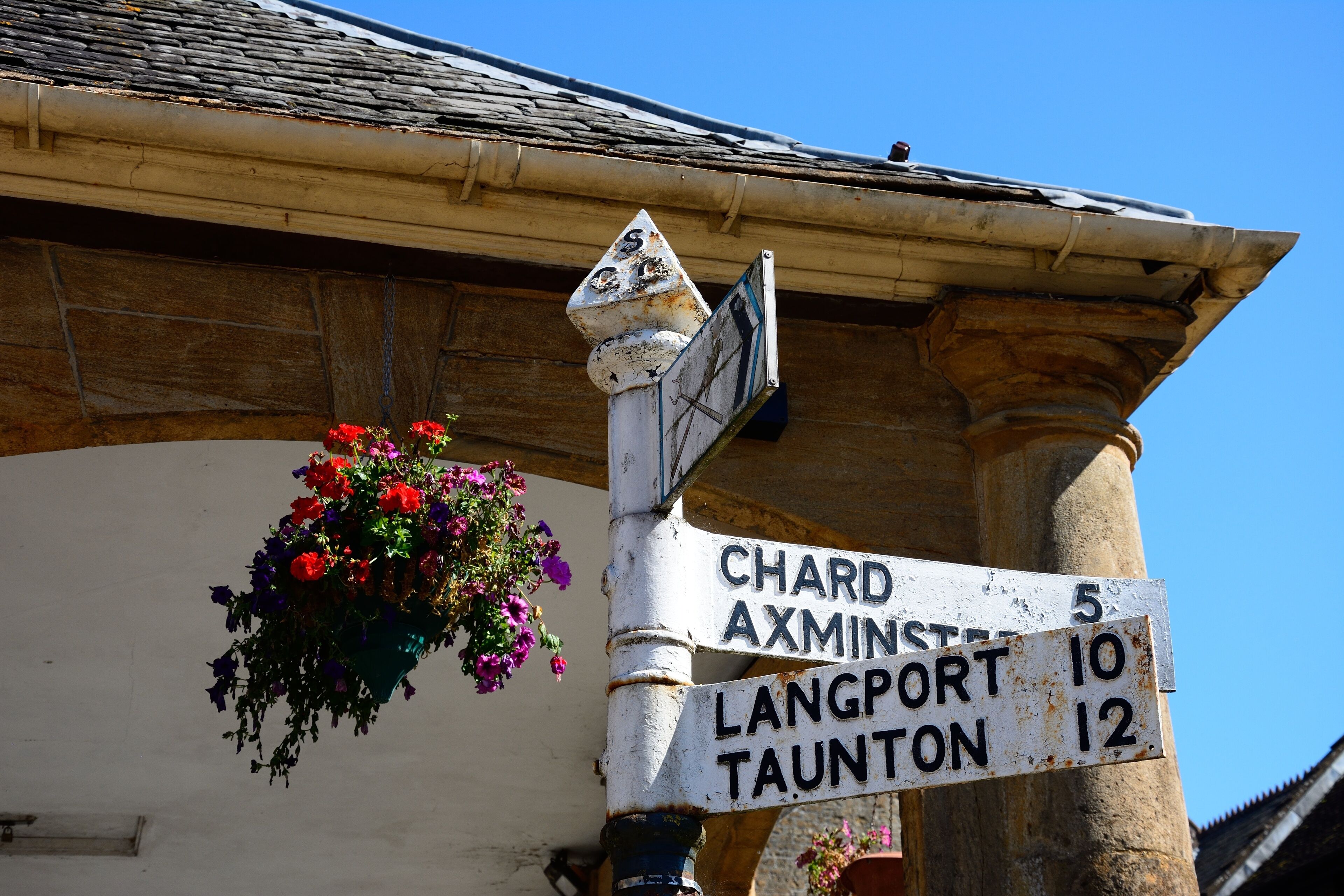 A weathered directional signpost with hanging flower baskets.