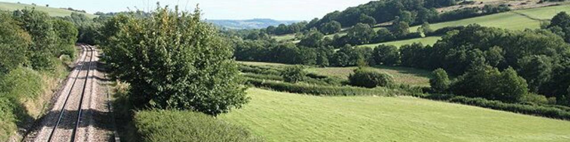 A railway track through a rural landscape with rolling hills and green fields.