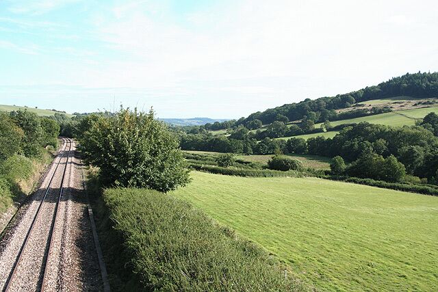 A railway track through a rural landscape with rolling hills and green fields.
