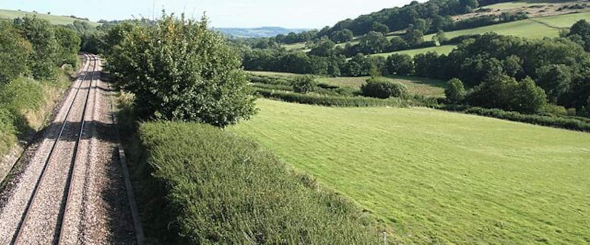 A railway track through a rural landscape with rolling hills and green fields.