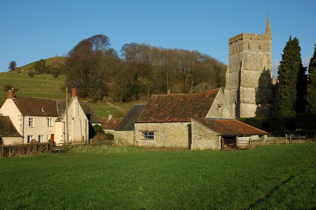 A rural village with stone houses, a church tower, and a grassy field.