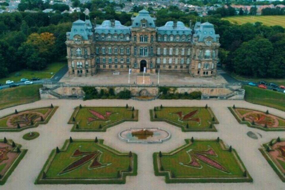 Een groot, historisch gebouw met een symmetrische tuinaanleg en een fontein in het midden.