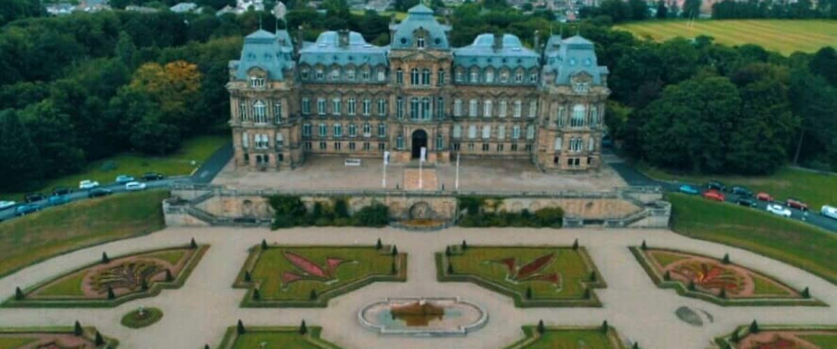 A large, historic building with a symmetrical garden layout and a central fountain.