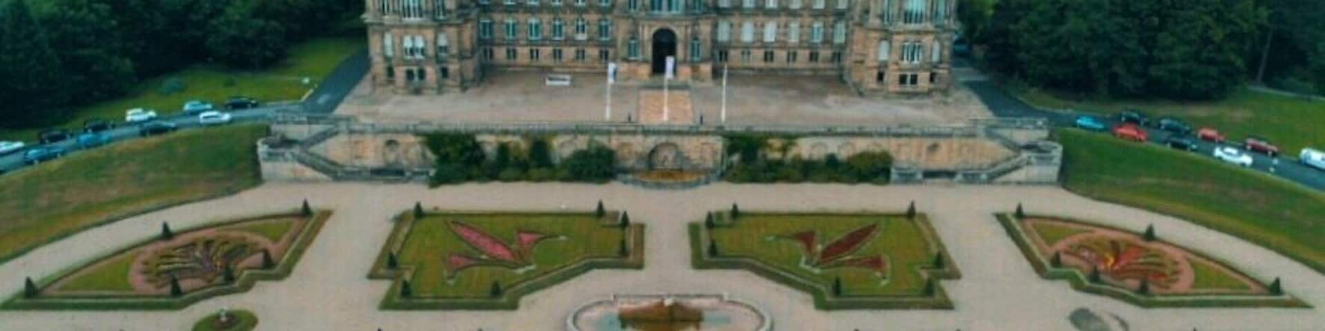 A large, historic building with a symmetrical garden layout and a central fountain.