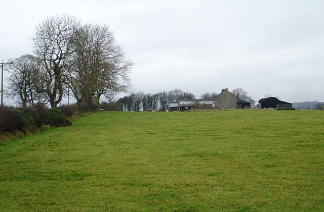 A rural landscape with a grassy field, a large tree, and several farm buildings in the background.