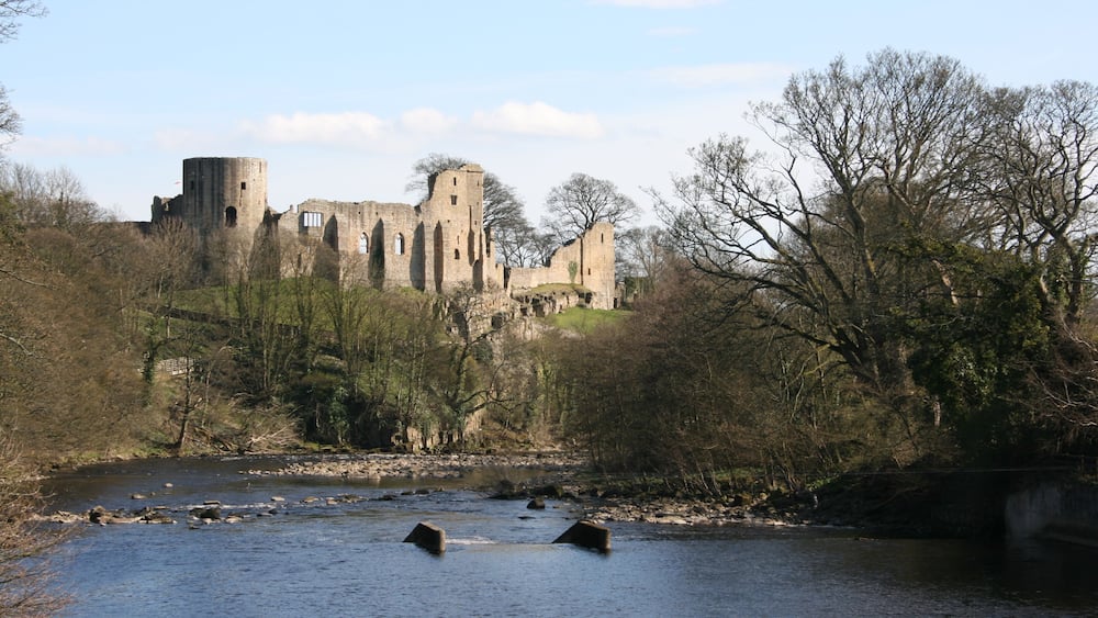 A historic castle by a river with ruins and trees.