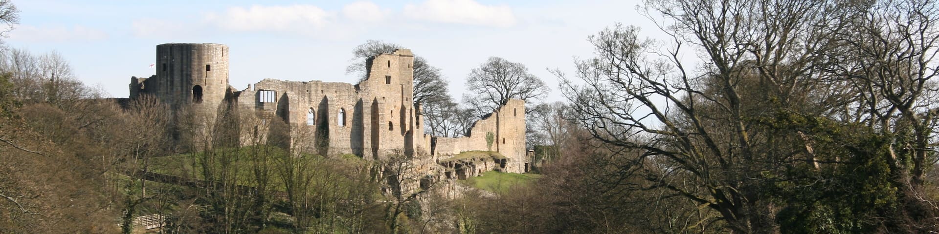 A historic castle by a river with ruins and trees.