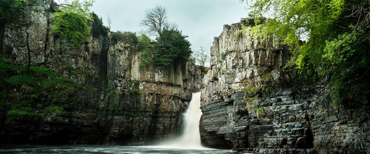 A waterfall cascading into a river surrounded by rocky cliffs and dense greenery.
