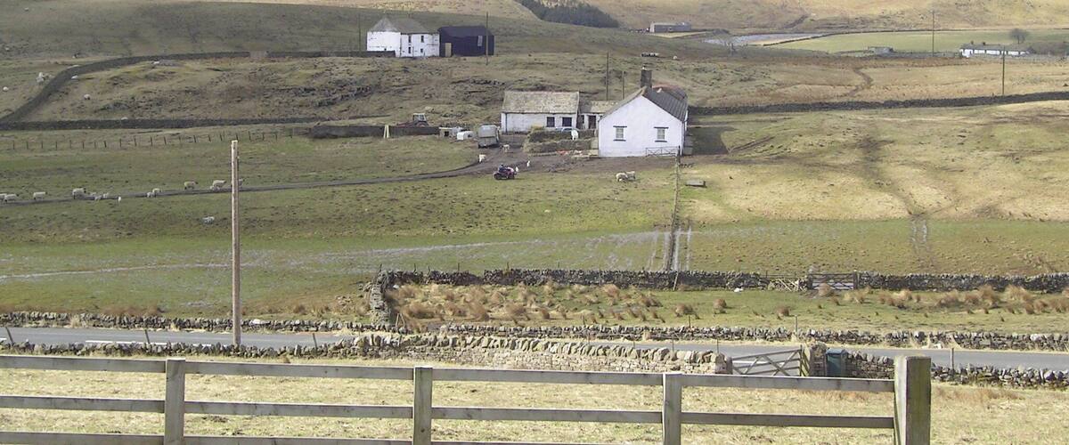 A rural landscape with rolling hills, a white house, and a stone wall.