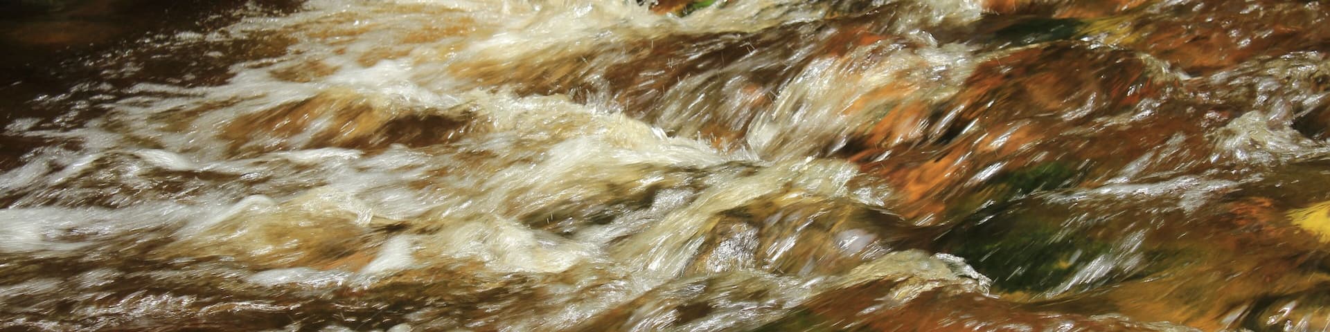 A fast-flowing river with clear water, surrounded by rocks and moss.