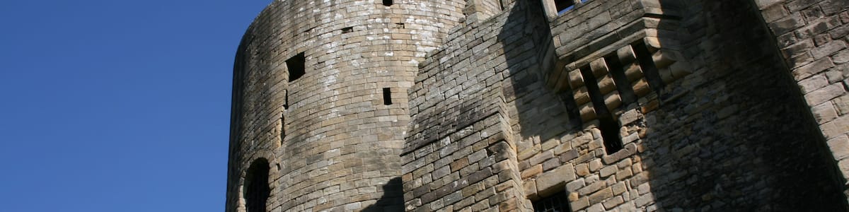 Ein steinerner Turm mit Rundbogenfenstern und einem grasbewachsenen Hügel.