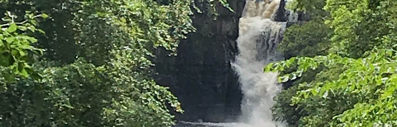 Un río fluye por un desfiladero rocoso, con una cascada al fondo.