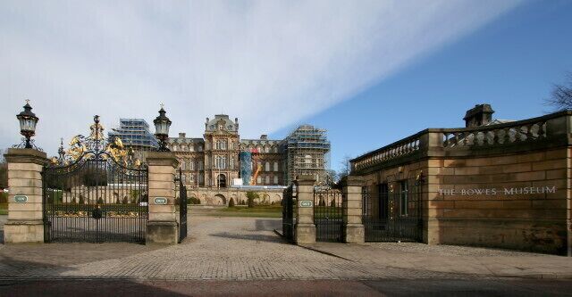 Entrada del Museo Bowes, con puertas ornamentales y un edificio grande al fondo.
