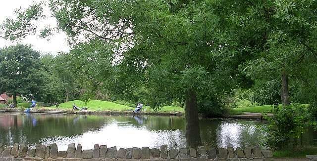 A calm river with stone walls, lush green trees, and a grassy bank.
