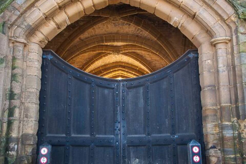 Un grand arc en pierre surmonté d’une porte en bois sombre.