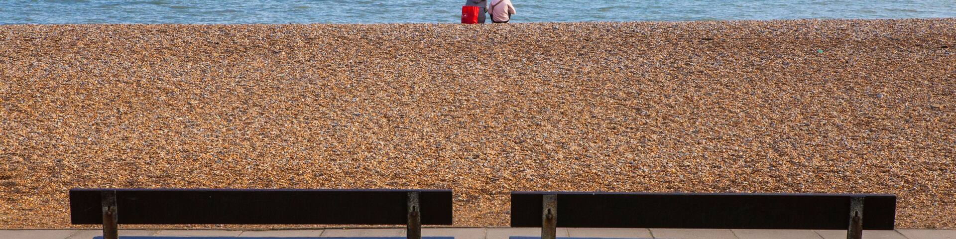 A pebbled beach with two benches facing the sea.
