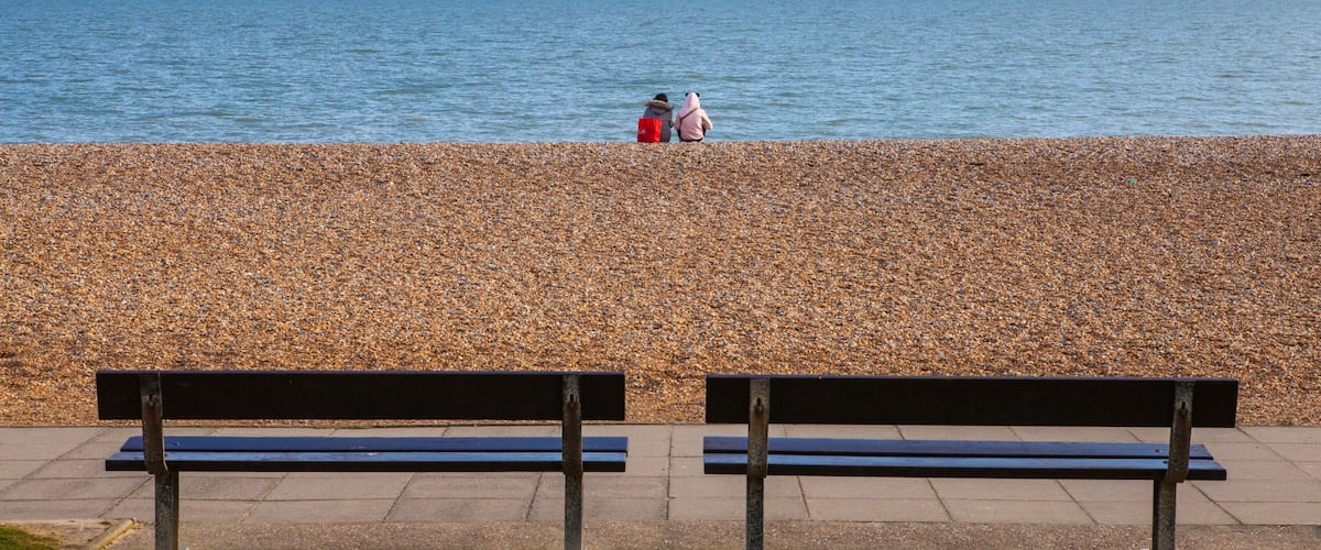 A pebbled beach with two benches facing the sea.