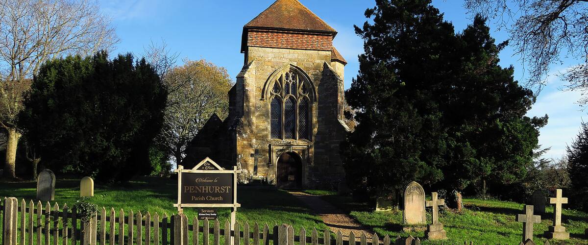 A historic church with a pointed roof and a weather vane, surrounded by a cemetery with headstones and a wooden fence.