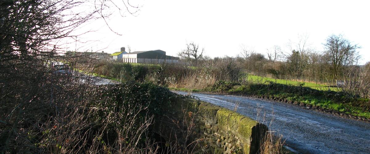 A rural road with a stone wall on one side and a grassy field on the other.