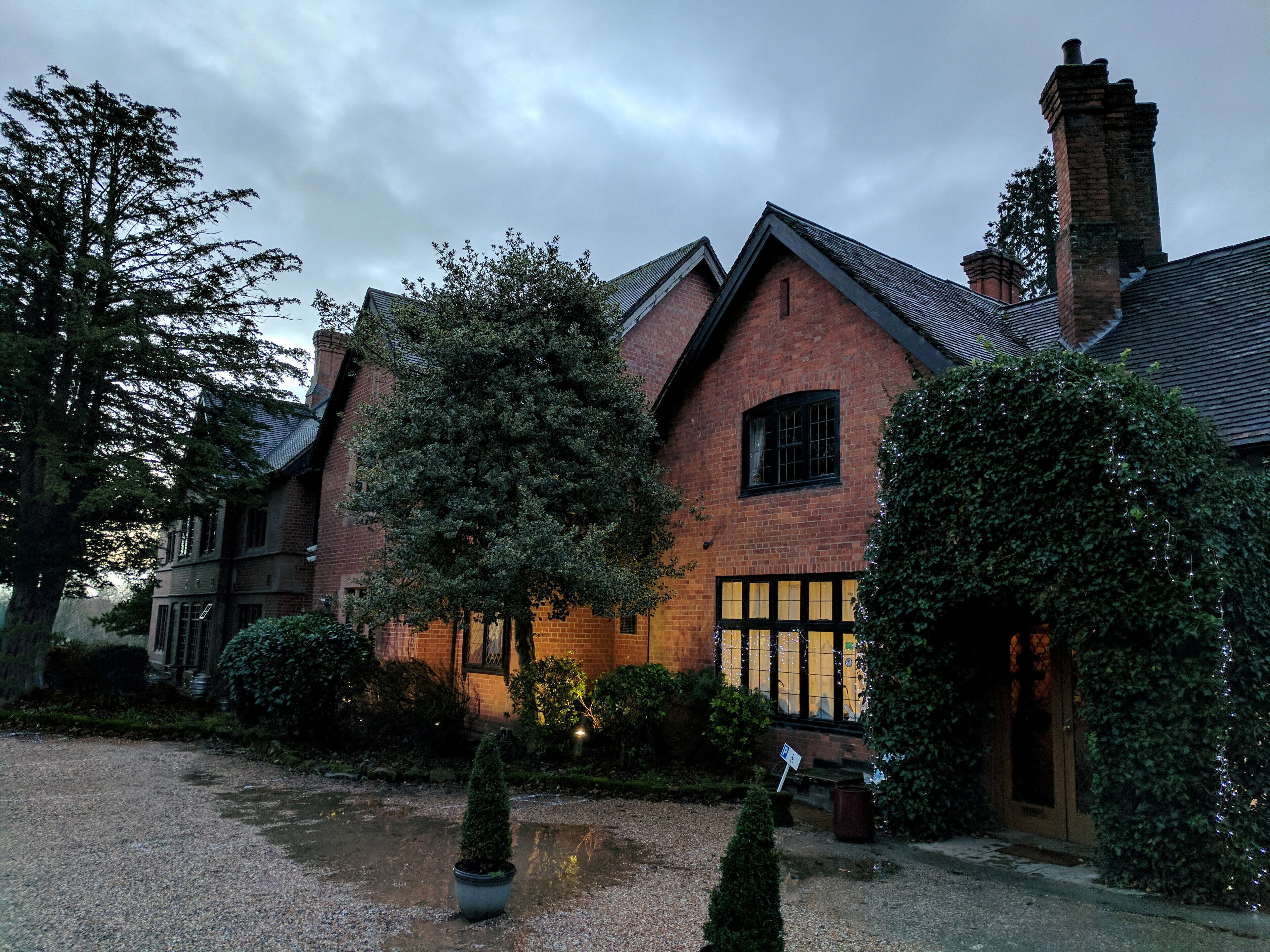 A brick house with a sloped roof and a large tree in front.