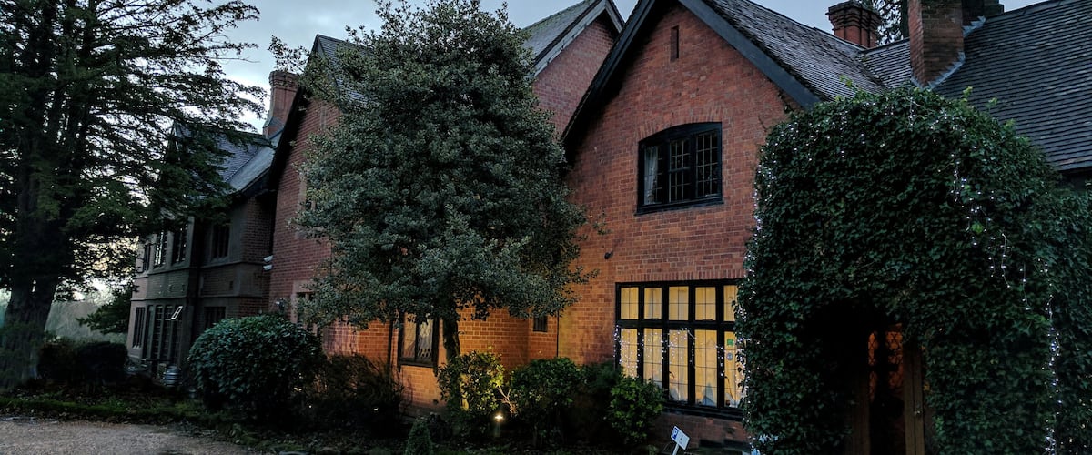 A brick house with a sloped roof and a large tree in front.