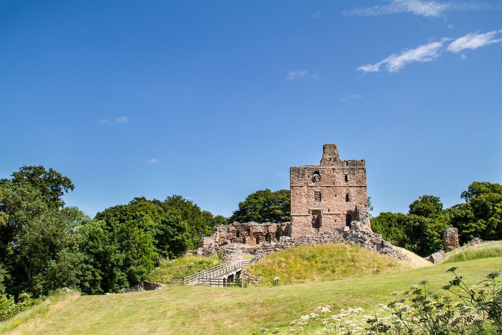A historic stone tower on a grassy hill with trees in the background.