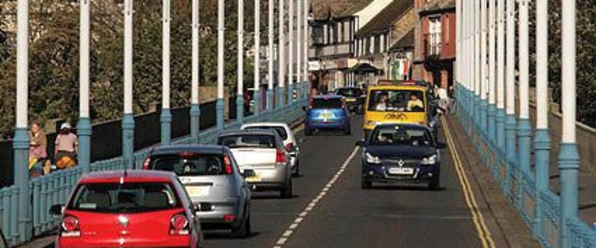 A bridge with street lamps, cars, and a church spire in the background.