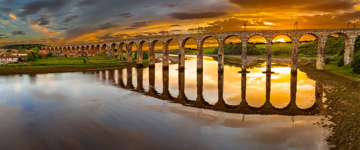 A stone viaduct spanning a river with a sunset reflection.