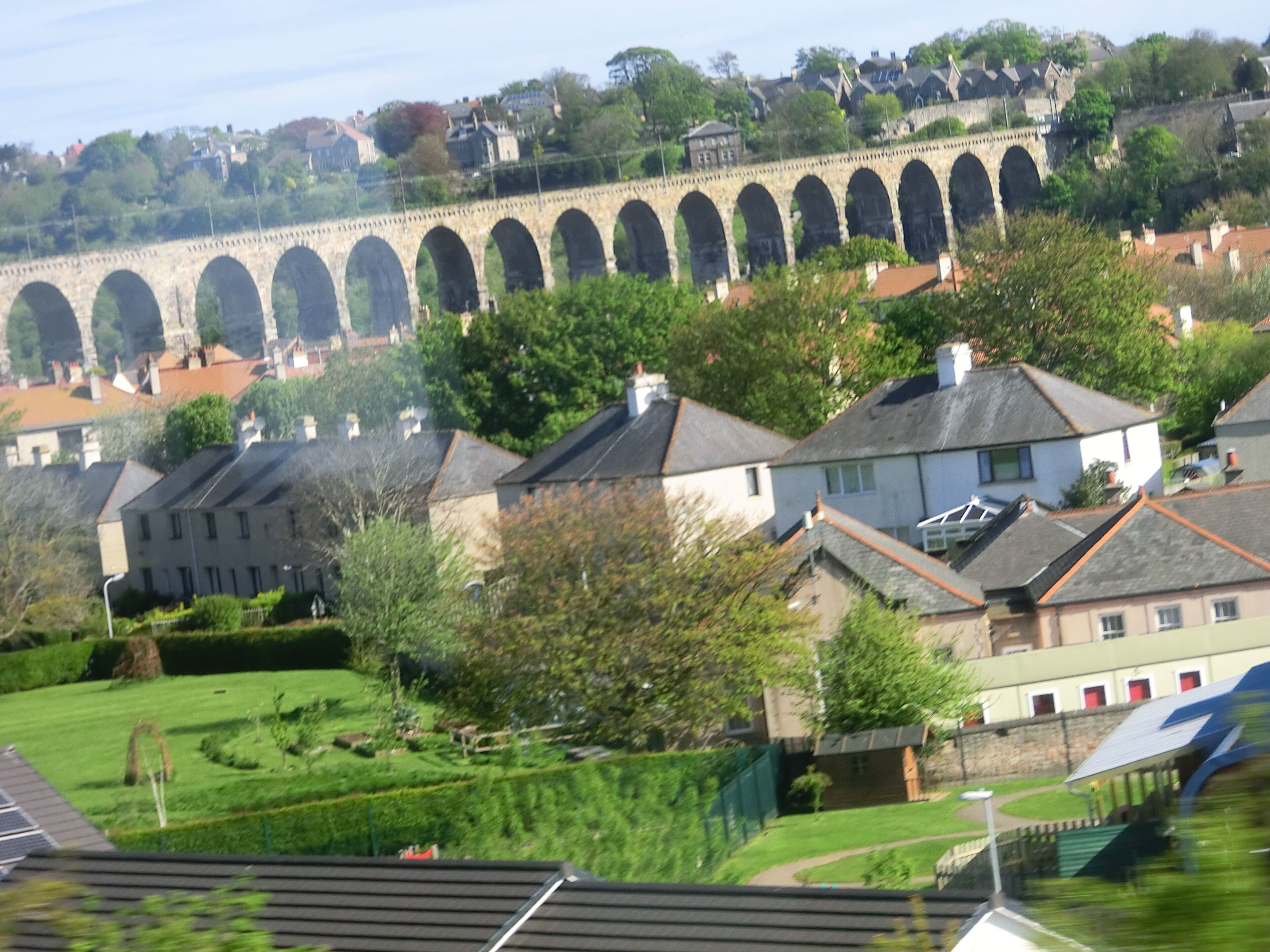 A stone viaduct with multiple arches, residential houses, and lush greenery in the foreground.