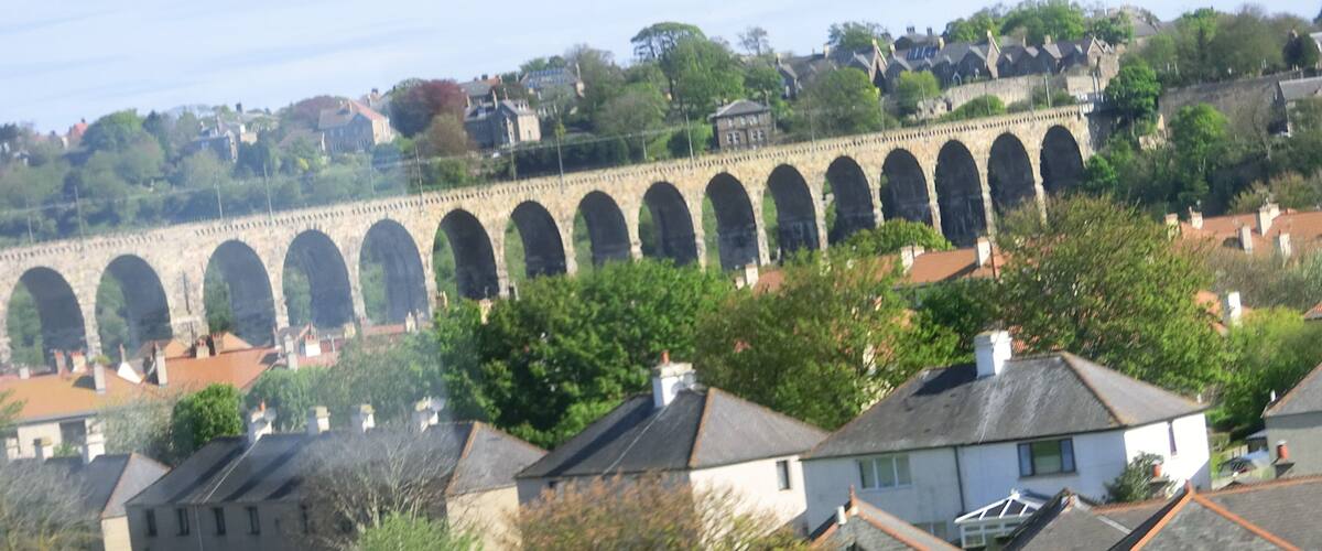 A stone viaduct with multiple arches, residential houses, and lush greenery in the foreground.