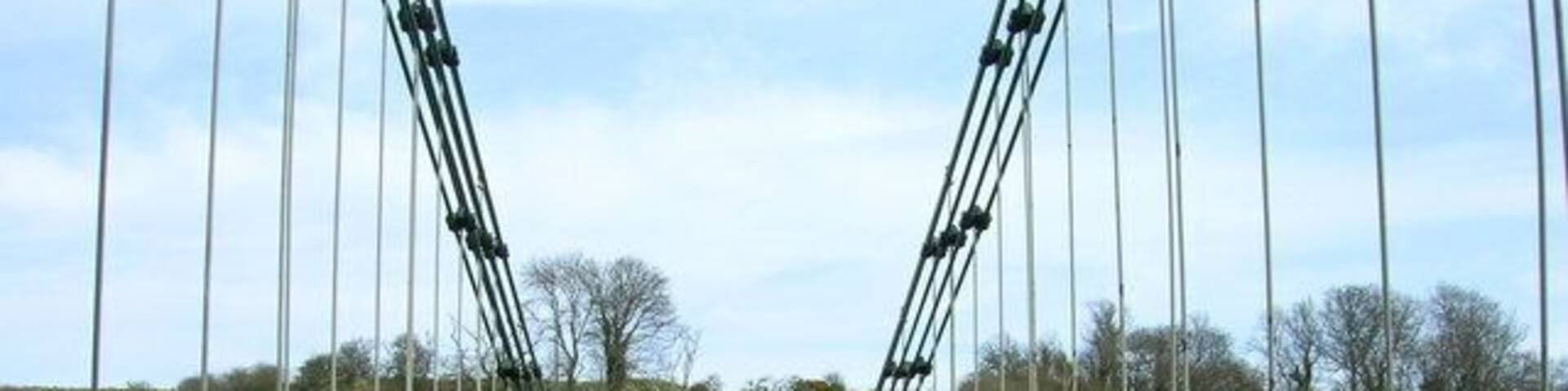 A suspension bridge with metal railings and a paved walkway over a river.