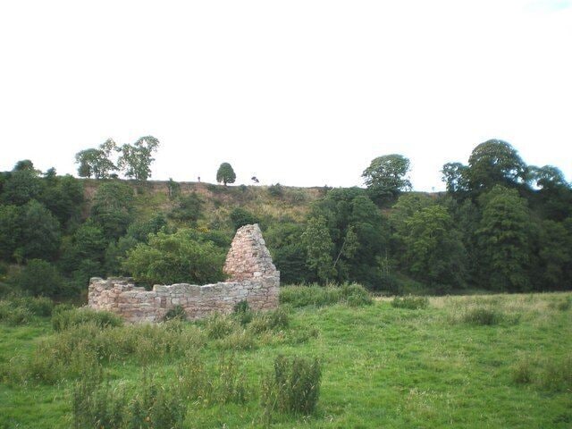 A stone ruin on a grassy hill with dense trees in the background.