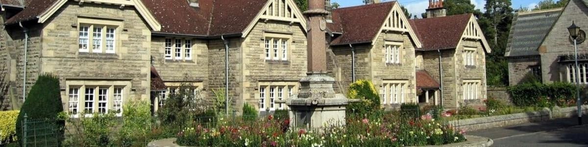 Ein Steins Denkmal mit einer Engelsstatue in einer dörflichen Umgebung mit traditionellen Steinhäusern und einem Blumenbeet im Vordergrund.