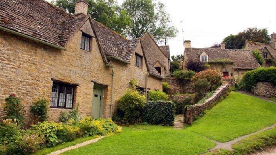 A quaint village with stone houses, a grassy courtyard, and a stone wall.