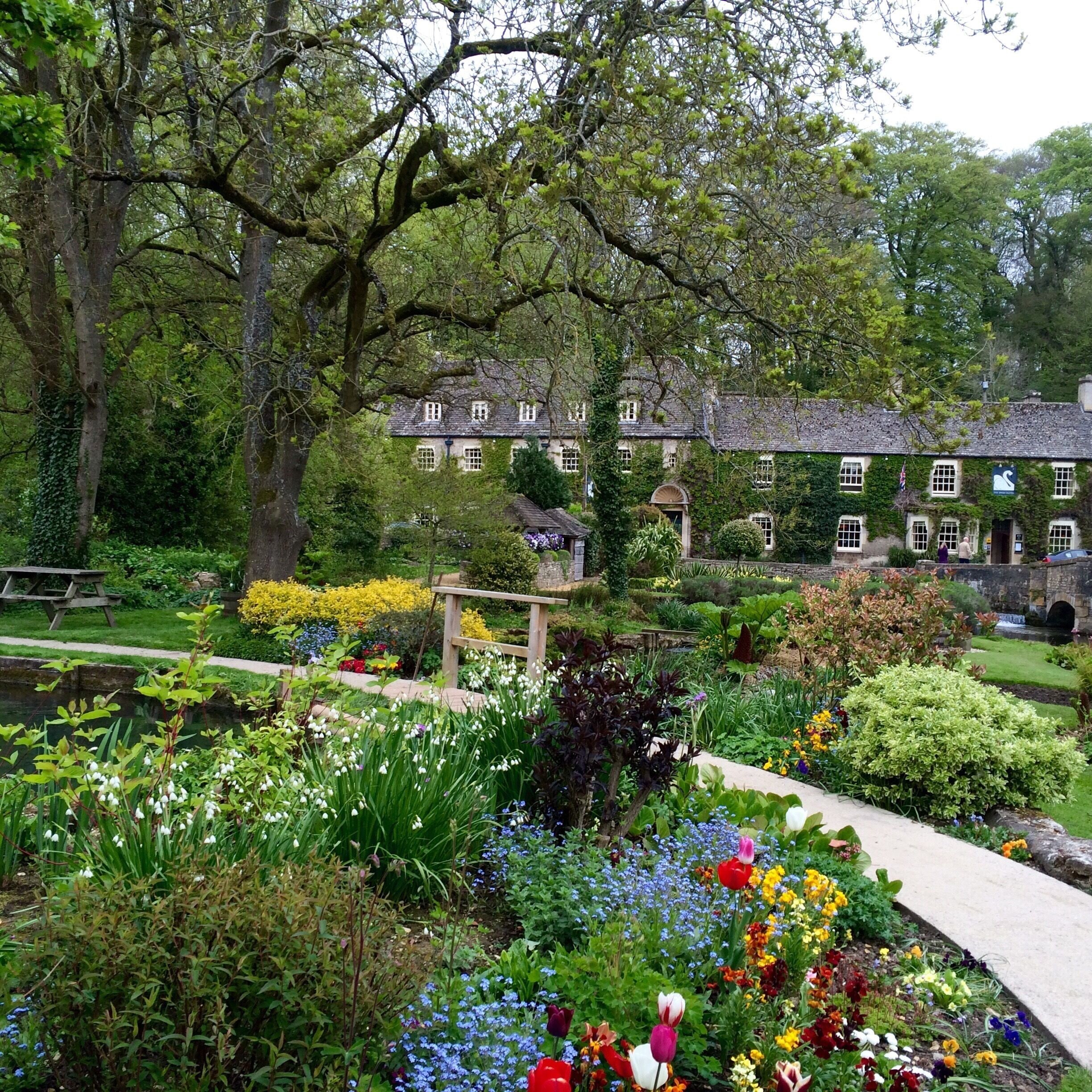 A lush garden with a variety of flowers, a stone bridge, and a historic building with ivy.