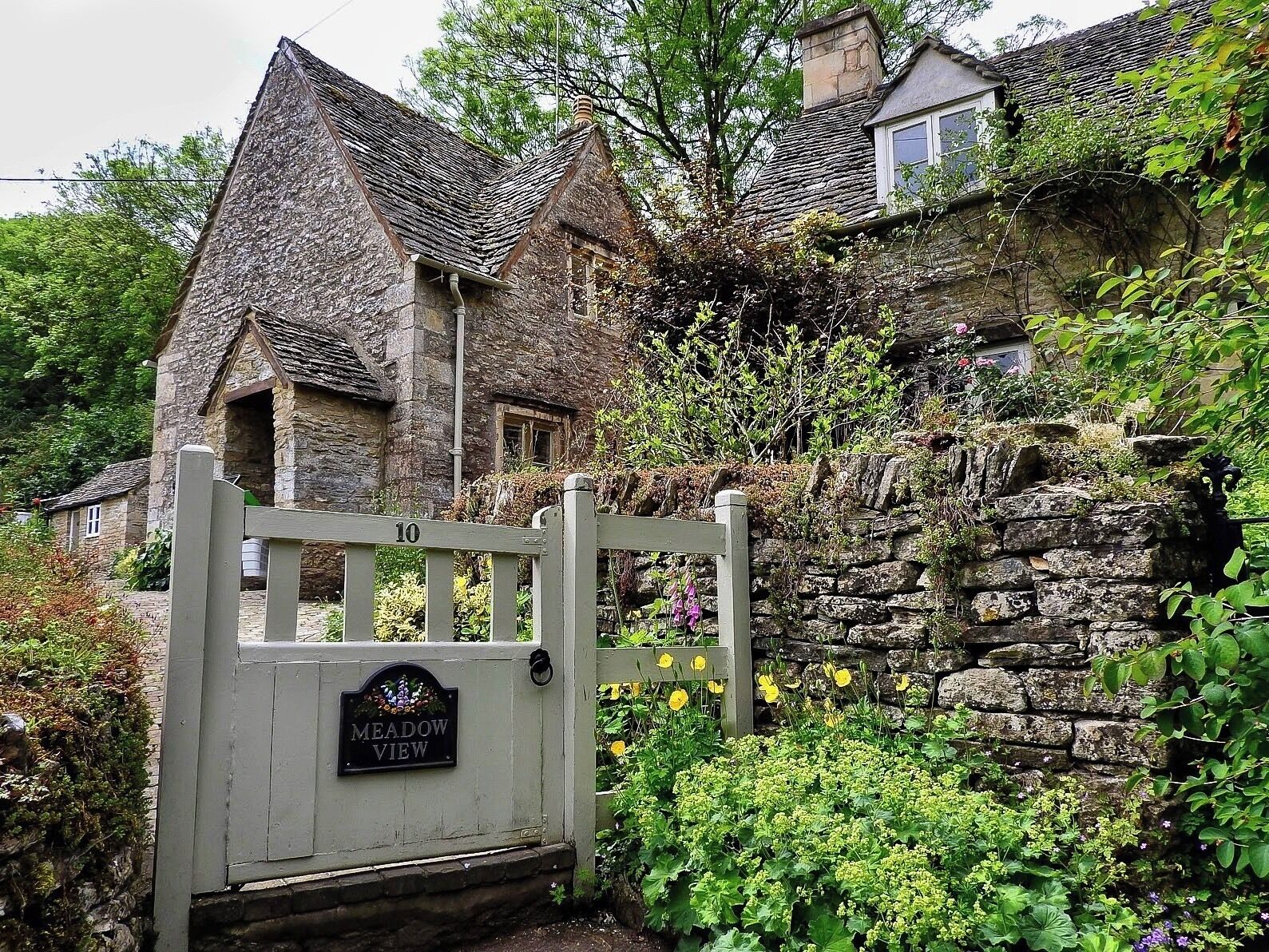 A stone house with a thatched roof, a wooden gate, and a sign reading "Meadow View".