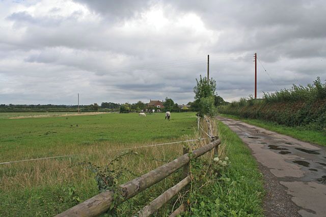 A rural landscape with a fence, a dirt path, and a green field.