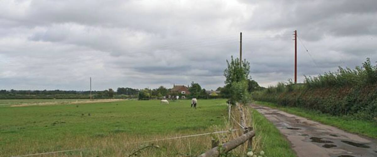 A rural landscape with a fence, a dirt path, and a green field.