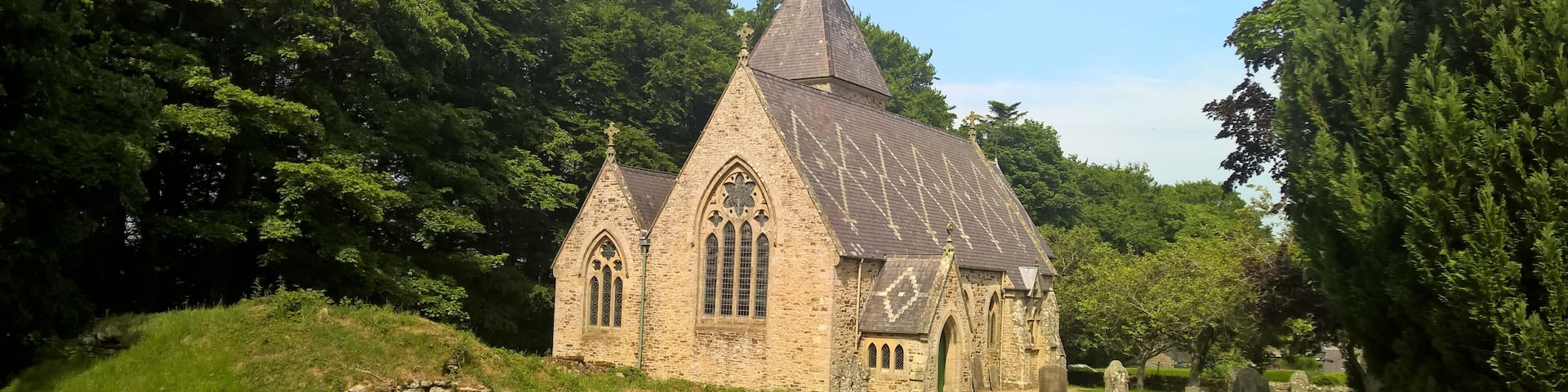 A small stone church with a pointed roof and a cross on top, surrounded by a cemetery with headstones.