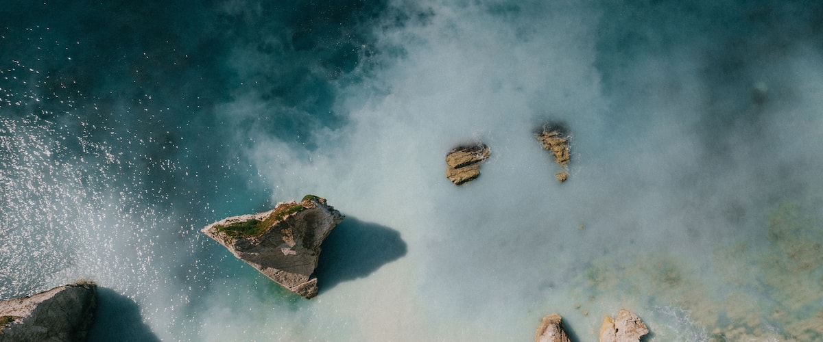 A coastal landscape with clear blue waters, rocky formations, and a small island with sparse vegetation.